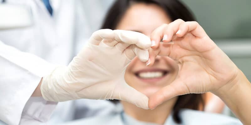 happy dental patient - heart hand sign with dentist