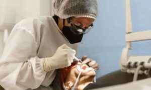 Healthcare worker in protective gear examining patient's teeth in clinical dental setting.