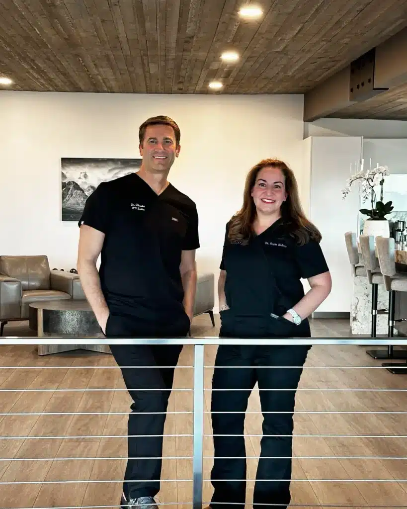 Two PV Smiles dental staff members stand behind reception counter in modern office.