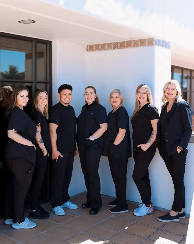 PV Smiles dental team members standing together in blue scrubs and shoes in modern office hallway.