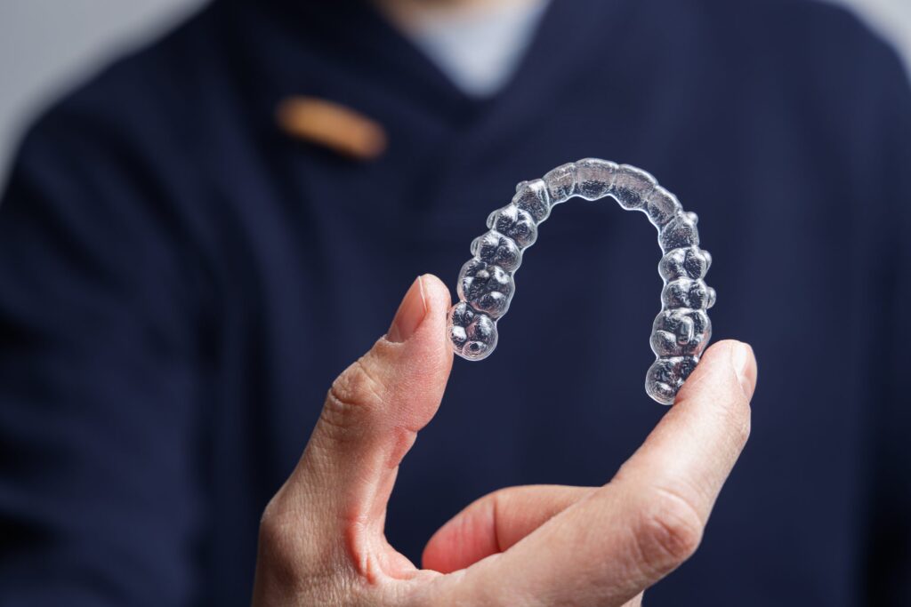 Person holding clear plastic dental aligner or retainer against blurred background