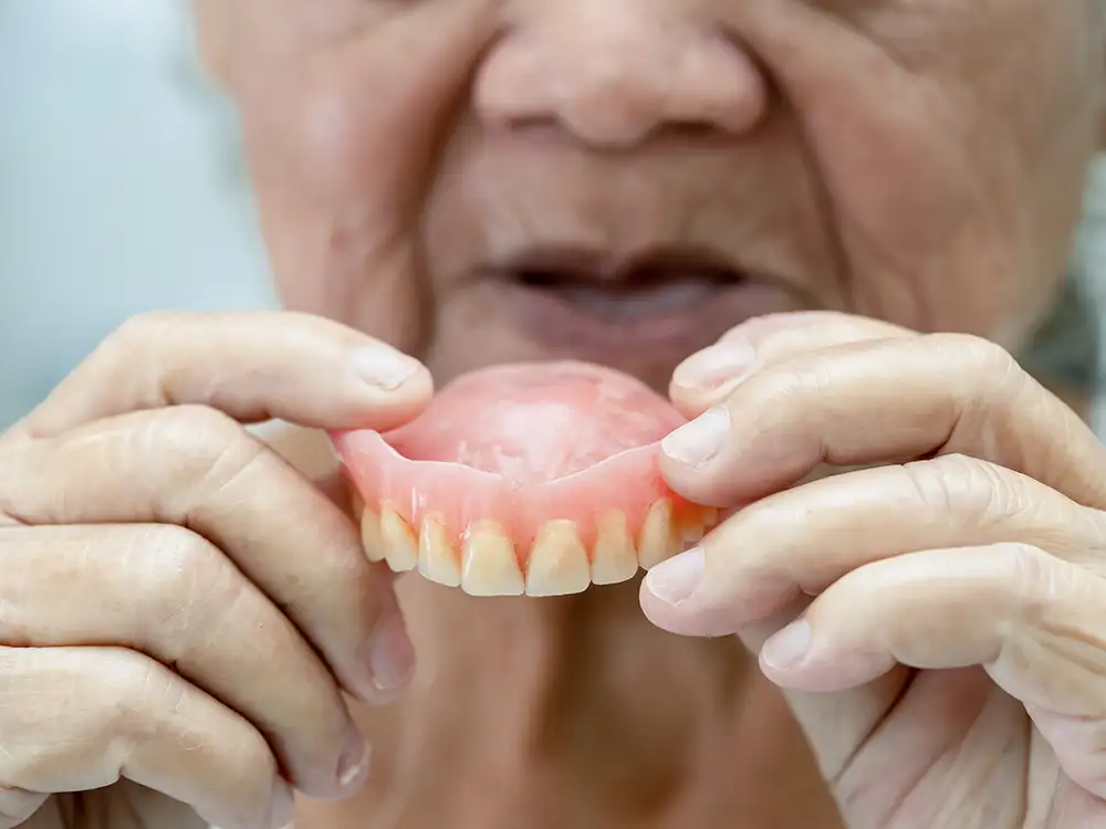 Older adult holding dentures in front of mouth, demonstrating dental prosthetics.