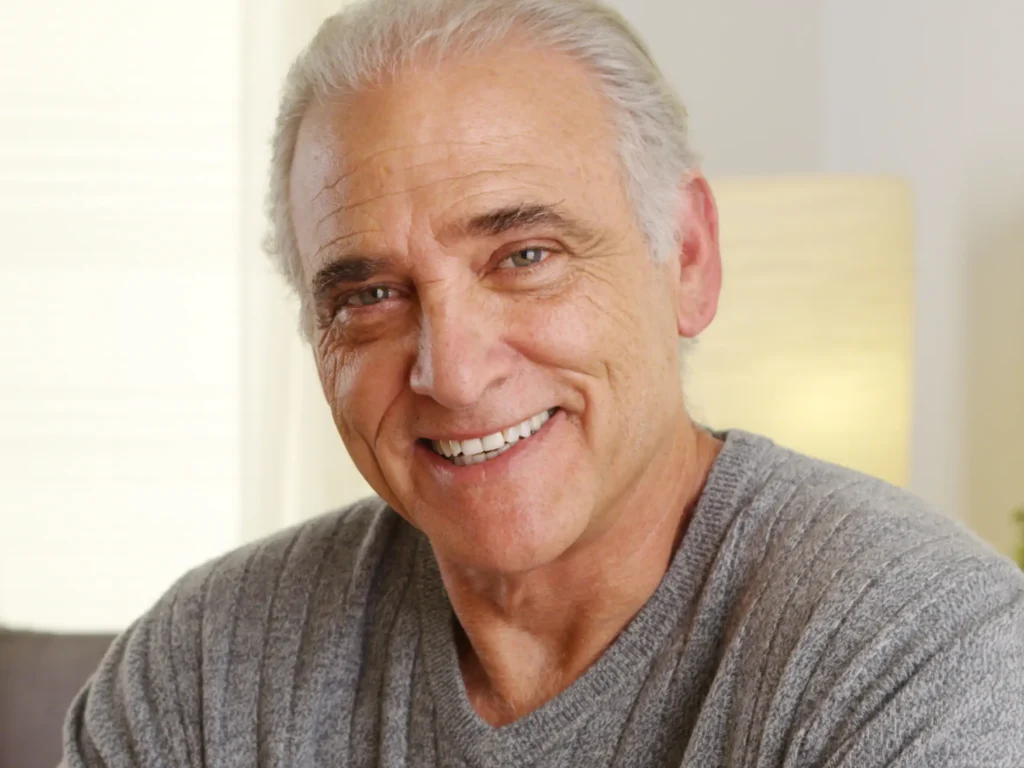 Smiling older man with gray hair wearing gray shirt against neutral background