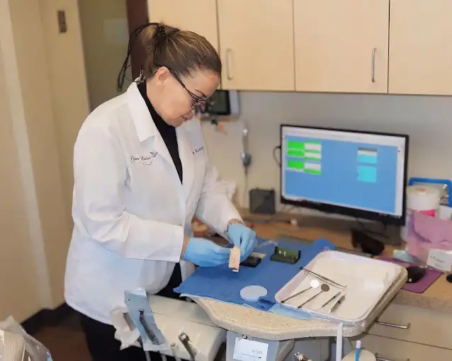 Healthcare professional in white coat working at medical workstation with computer monitor and blue equipment.