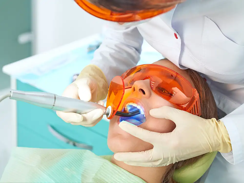 Dentist in protective gear examining child's teeth with dental tools in clinical setting.