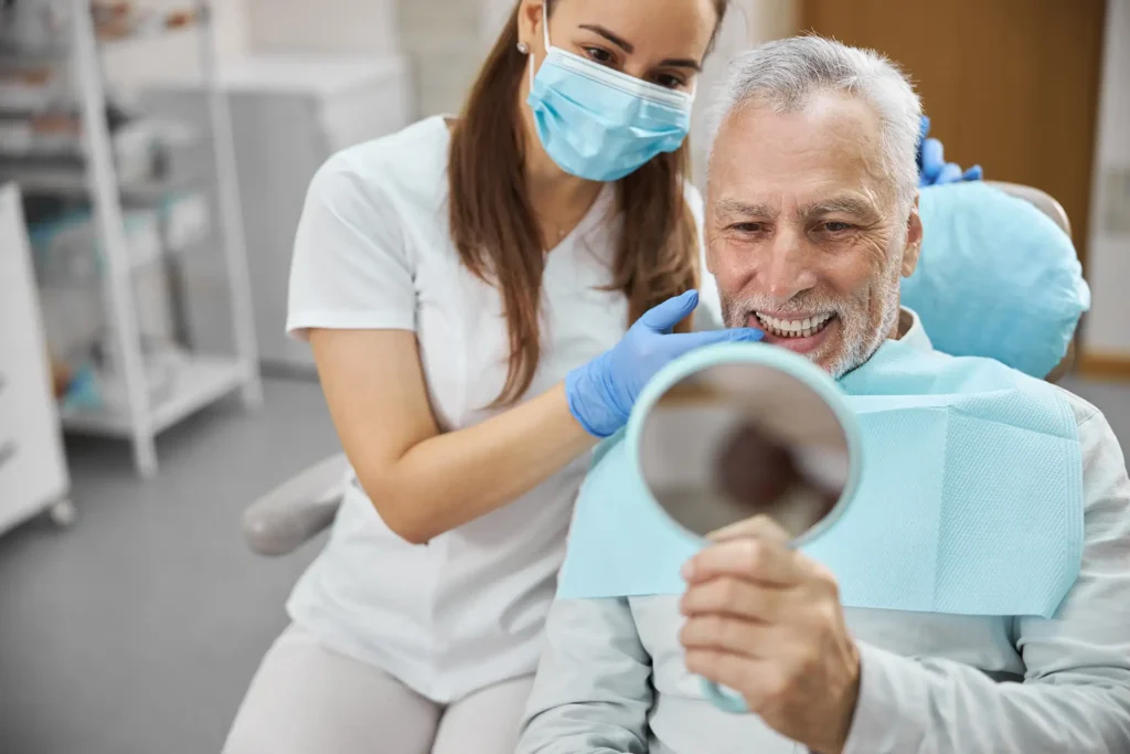 Senior man examining dental X-ray with female dentist in mask at dental clinic.