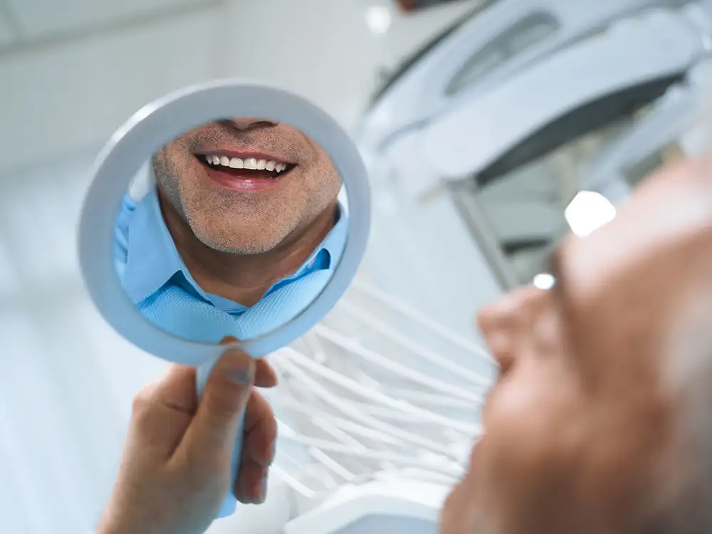 Dentist in blue gloves holding mirror reflecting patient's smile during dental examination.