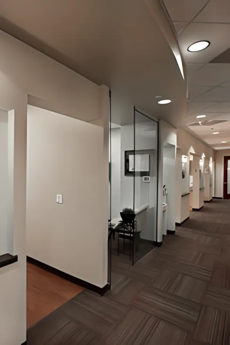 Modern office corridor with glass-walled meeting rooms and recessed lighting along hallway.
