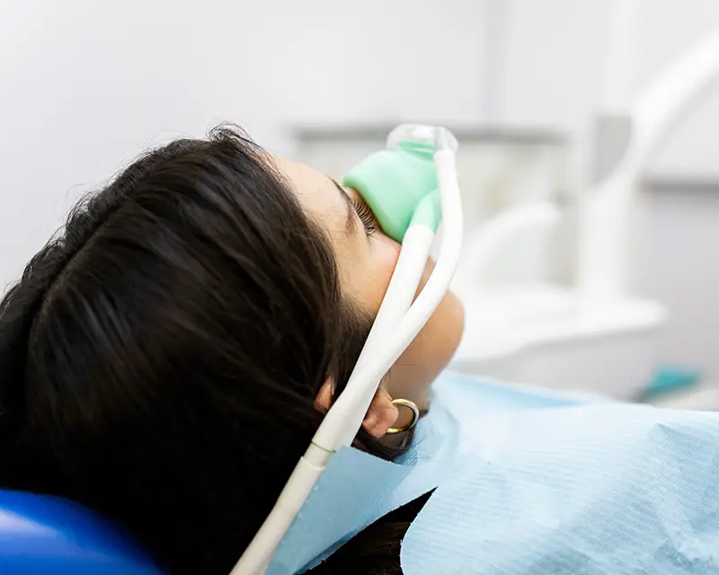 Patient receiving dental treatment in modern dental office, wearing protective mask and bib.