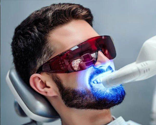 Man receiving blue light teeth whitening treatment at dental clinic wearing protective eyewear