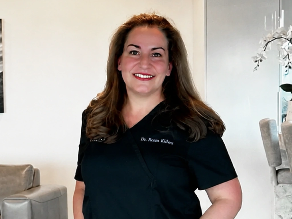 Smiling woman in black scrubs standing in a bright clinic environment.